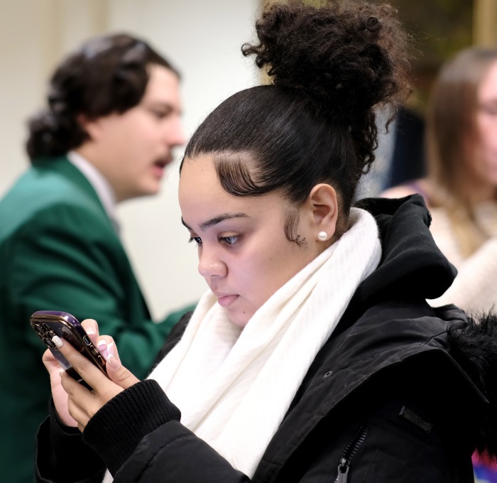 Female student in coat looking at cell phone with students in background