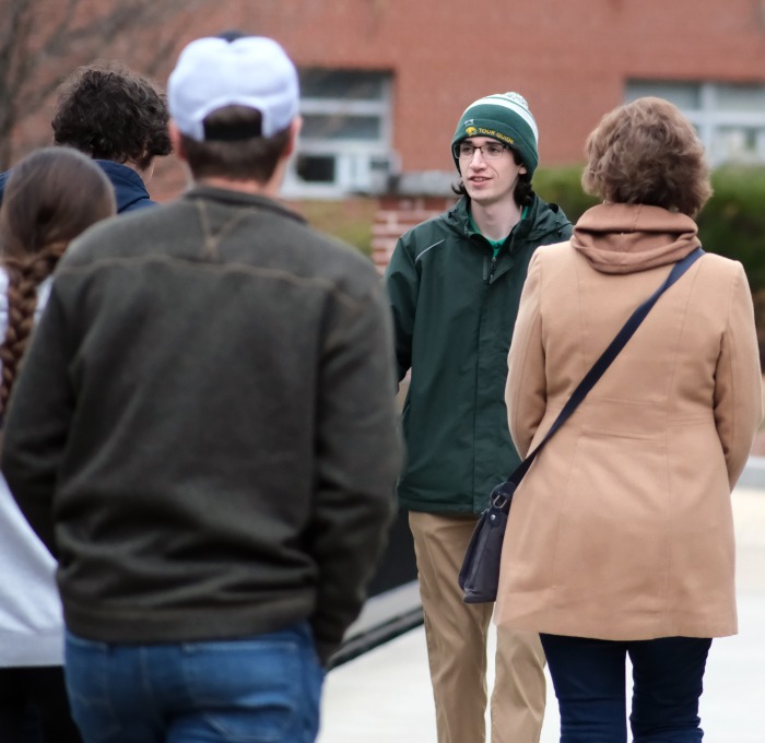 Tour guide walking backwards giving tour to group on quad