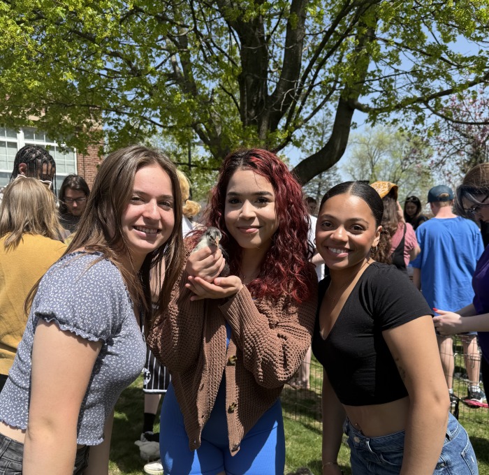 Students posing and smiling with duck on quad