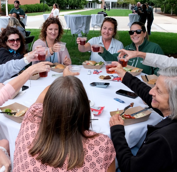 Admin staff on quad at bbq smiling and raising their glasses in a toast