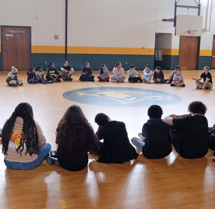 Future falcon academy students sitting on the floor in gym with police students