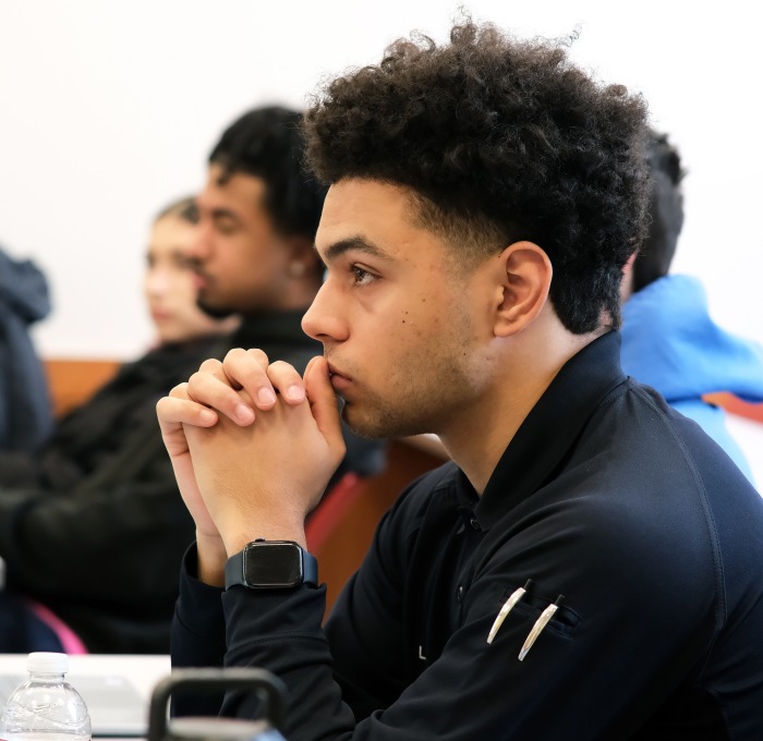 Male student with hands clasped in front of his face focusing in classroom.