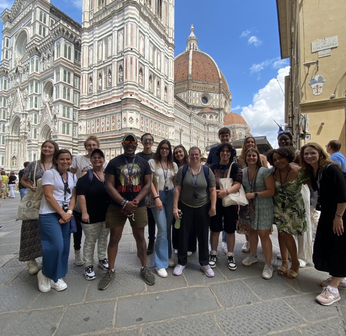 Group of students and staff in Verona Italy with white buildings in background.