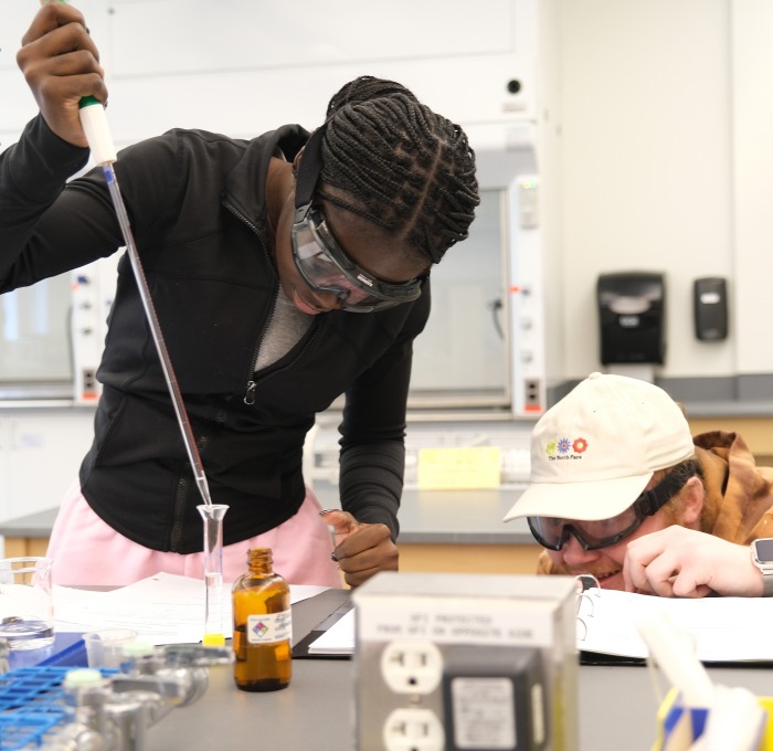 Female and male student pouring chemicals into a beaker in chemistry lab