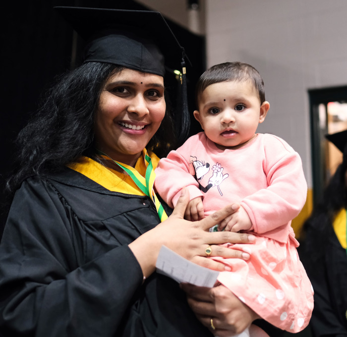 Graduate smiling with child in rec center.