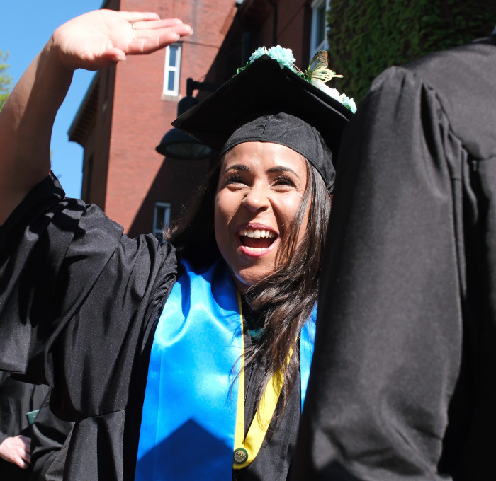 Smiling female student waving at commencement.