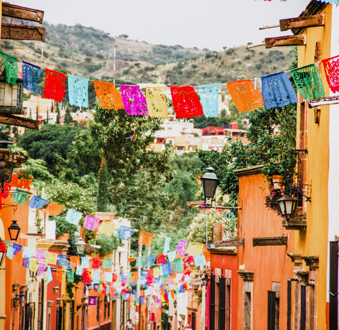 Spanish street with buildings, flags, and mountain in the background.