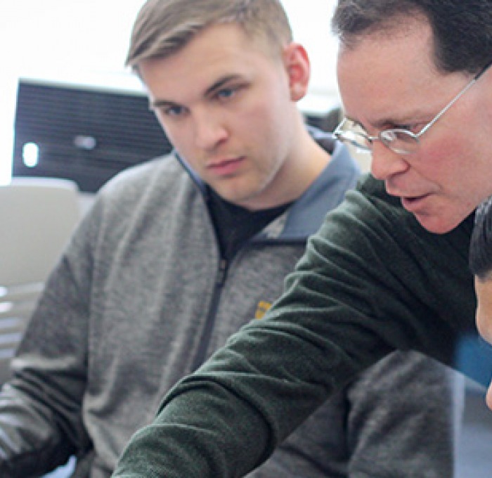 Professor helping students at a laptop in a classroom