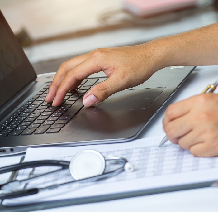 Nursing student hands typing on a laptop with stethoscope next to it