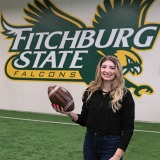 Linnea D’Acchille ‘22 standing with football in Fitchburg State training facility