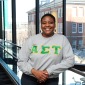 Female student smiling in library near windows with campus building in background