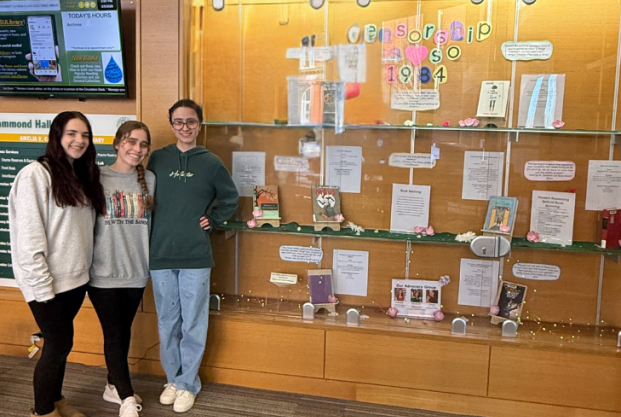 Three people stand smiling in front of a glass display case featuring books and posters about censorship, with the words "Censorship in 1984" written at the top of the display.