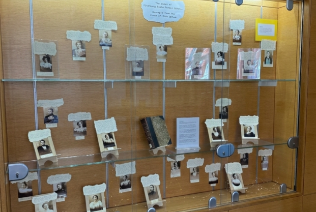 Glass display cabinet with historical photos and a book, alongside descriptive placards.