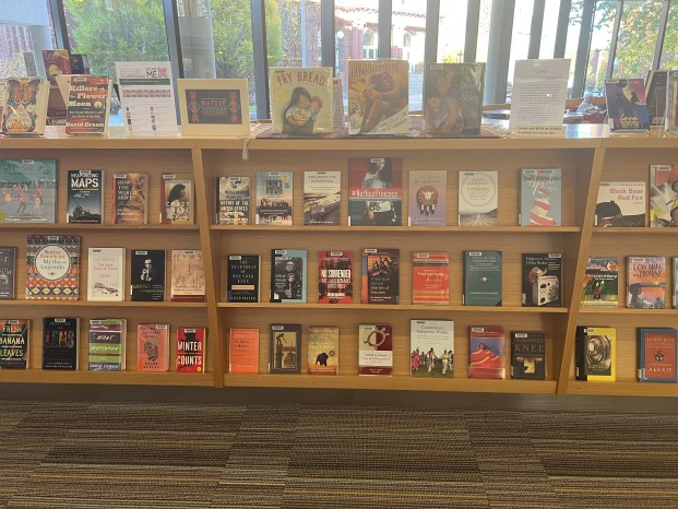 Print books on display on several book shelves in front of a large window. The books are all on various aspects of Native American culture and history.