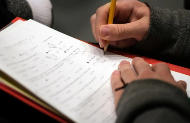 Close up of math test with hands and pencil.