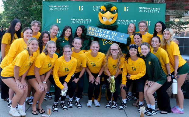 Female soccer players with Freddy in front of the green monster on quad.
