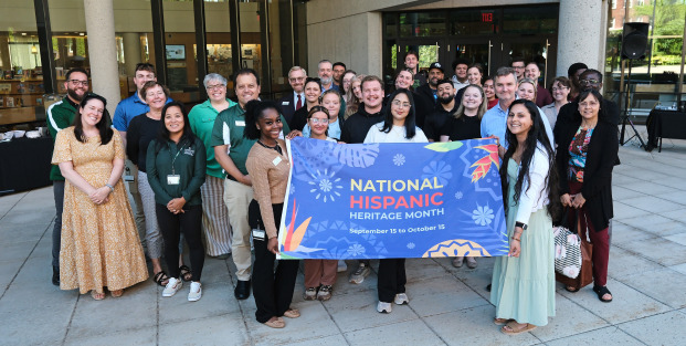 Krysta and student holding National Hispanic Heritage Month flag with group on alumni quad before flag raising.