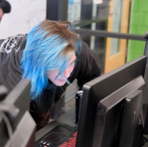 Student with blue hair on desktop computer in classroom