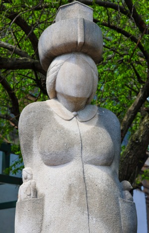 The Immigrant sculpture of woman with boat hat and people in pockets 