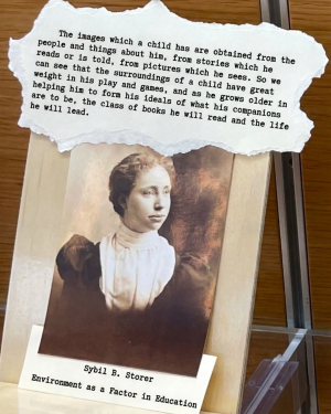Old photograph of a young woman with a typewritten quote above it. The display is labeled with “Sybil B. Storer” and “Environment as a Factor in Education.”