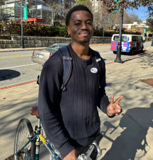 Student in front of van with I voted sticker giving peace sign.