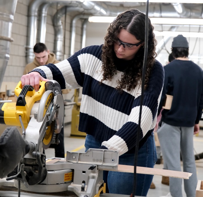 Female student using saw in design and fabrication class